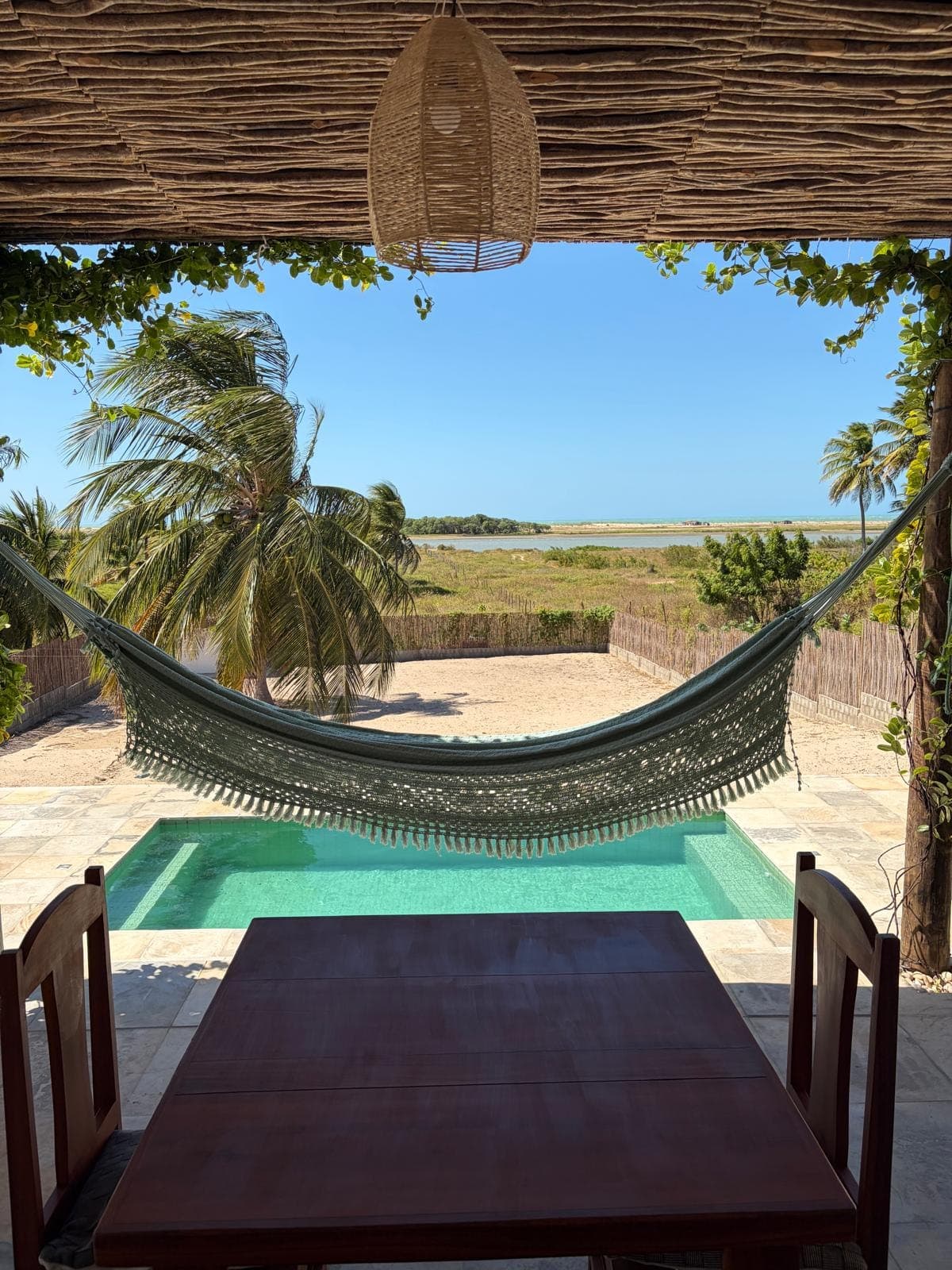 Hamac tendu sous le toit de branches, face à la piscine et à la lagune