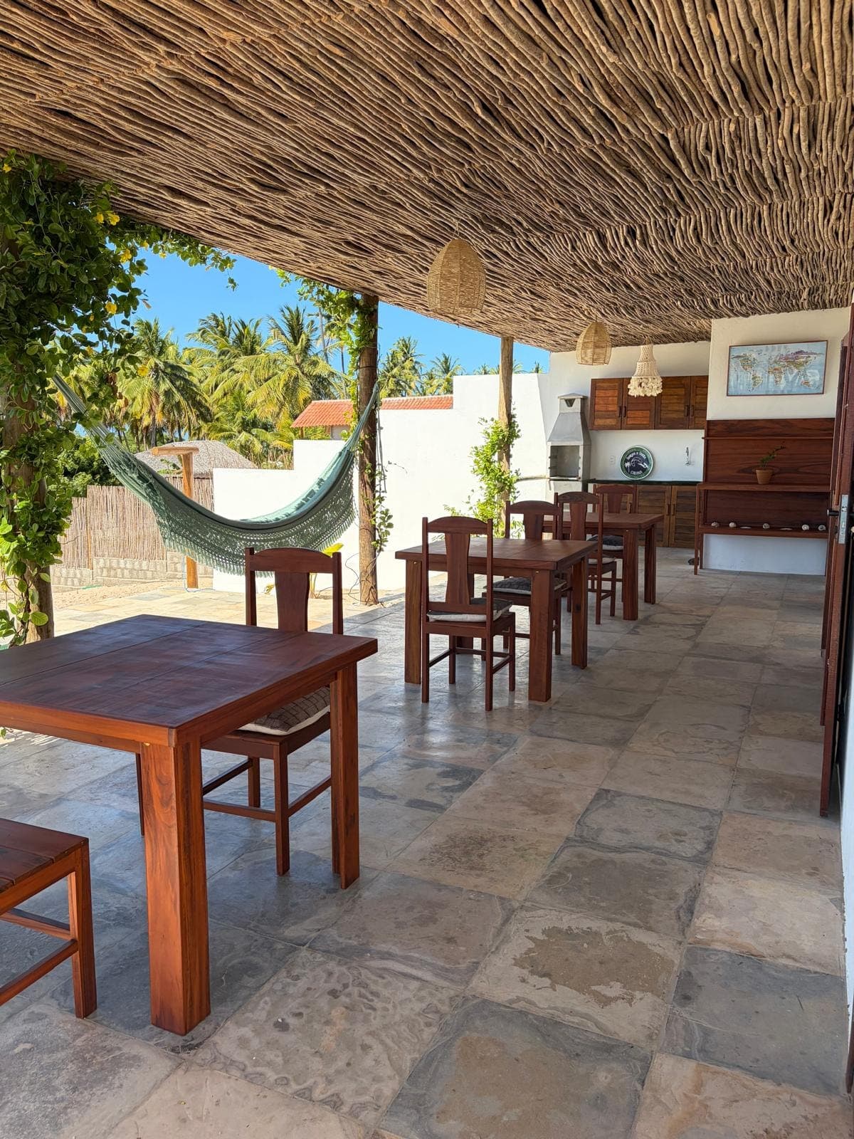 Terrasse couverte, ses tables en bois et son hamac, sous un toit de branches